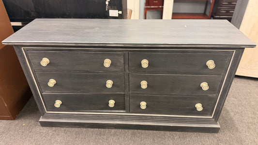A six-drawer double dresser in a distressed charcoal black finish framed with light pinstripe bordering and ornate round brass-finish pull knobs in good condition.