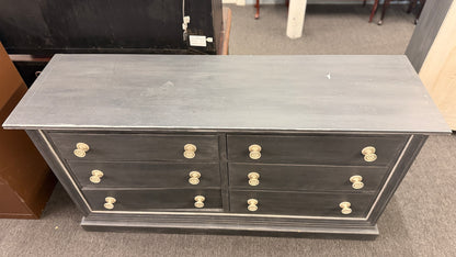 A six-drawer double dresser in a distressed charcoal black finish framed with light pinstripe bordering and ornate round brass-finish pull knobs in good condition.