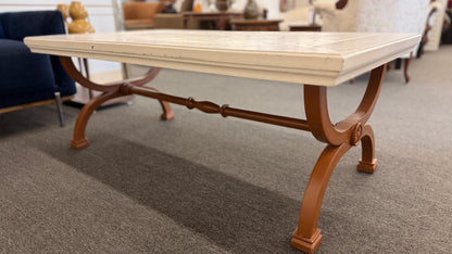 A rectangular coffee table featuring a distressed painted white top supported by an arched reddish-brown wood base with a central stretcher.