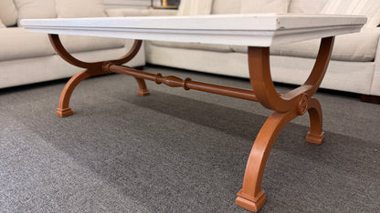 A rectangular coffee table featuring a distressed painted white top supported by an arched reddish-brown wood base with a central stretcher.