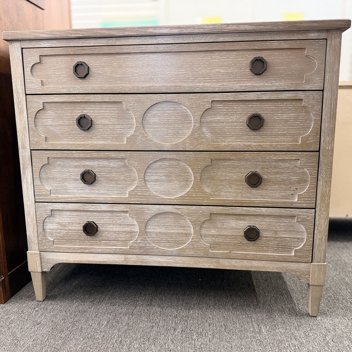 Distressed wood four-drawer chest featuring raised geometric drawer fronts, dark octagonal ring pulls, and a light washed finish.