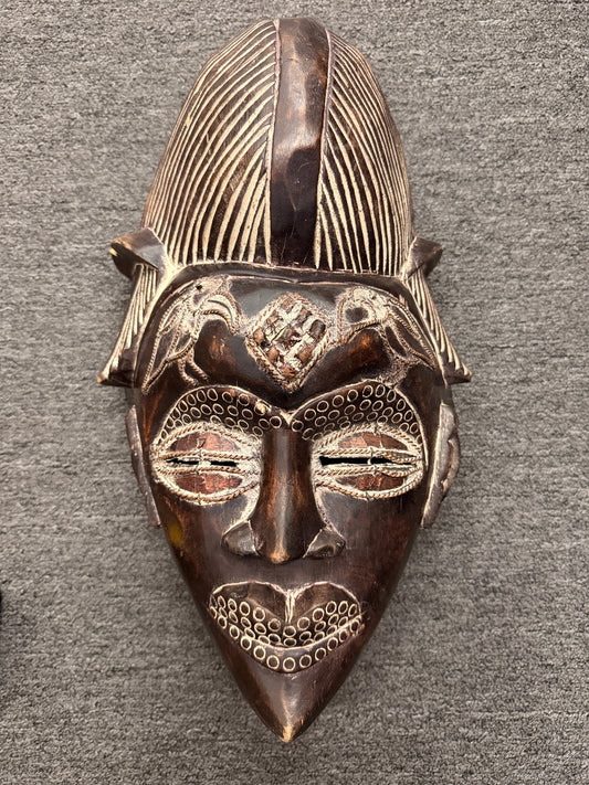 An elongated tribal-style carved wooden wall mask detailed with geometric linework, textured dot patterns, and light pigment accents in excellent condition.