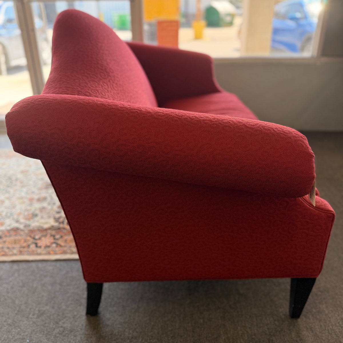 A bright red upholstered Ethan Allen loveseat with a subtly patterned fabric, curved backrest, and dark tapered legs in good condition.
