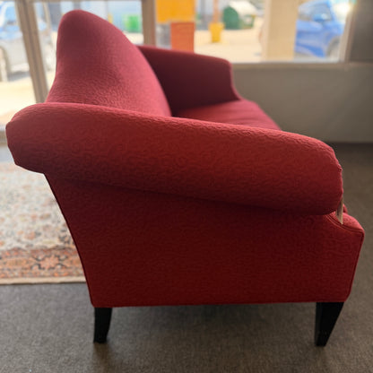 A bright red upholstered Ethan Allen loveseat with a subtly patterned fabric, curved backrest, and dark tapered legs in good condition.