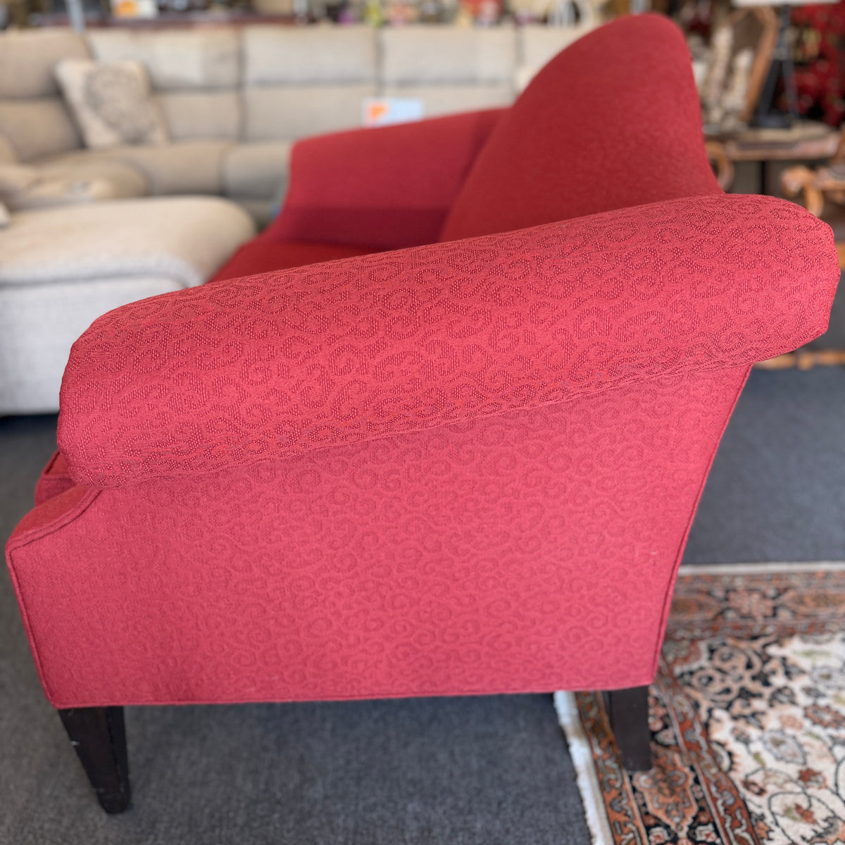 A bright red upholstered Ethan Allen loveseat with a subtly patterned fabric, curved backrest, and dark tapered legs in good condition.