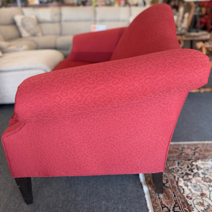 A bright red upholstered Ethan Allen loveseat with a subtly patterned fabric, curved backrest, and dark tapered legs in good condition.