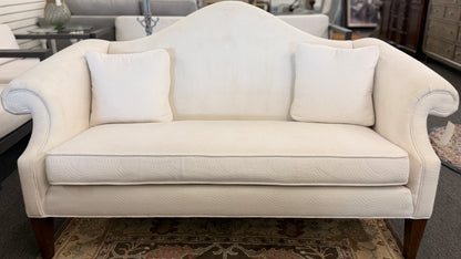Cream upholstered Ethan Allen camelback loveseat featuring rolled arms, a single seat cushion, two matching throw pillows, and dark tapered wooden legs.