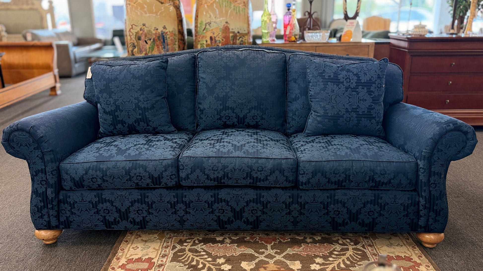 Traditional Ethan Allen three-seater sofa upholstered in blue tone-on-tone damask fabric with English rolled arms, three seat cushions, three back cushions, two matching accent pillows, and turned wooden bun feet.