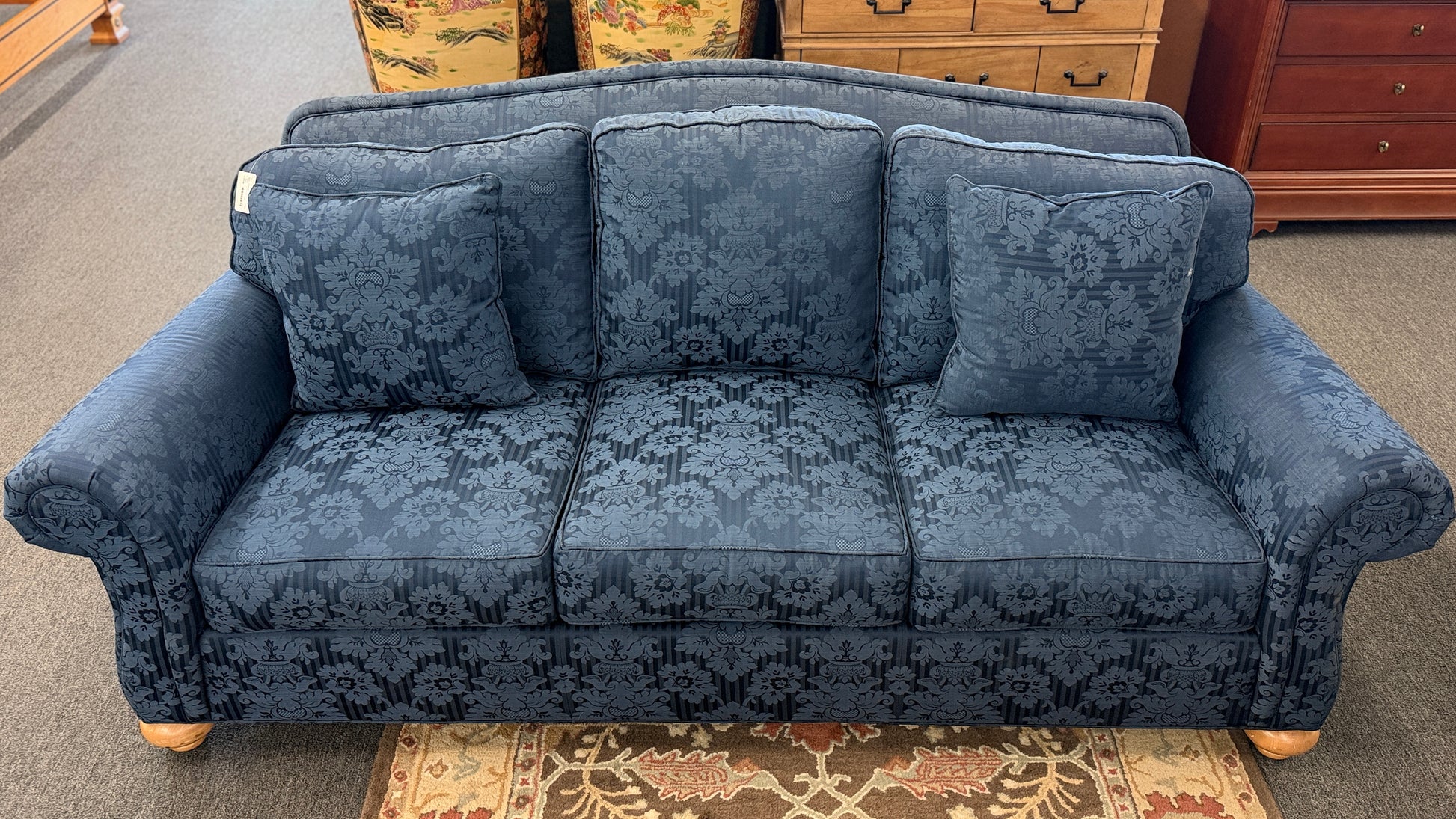 Traditional Ethan Allen three-seater sofa upholstered in blue tone-on-tone damask fabric with English rolled arms, three seat cushions, three back cushions, two matching accent pillows, and turned wooden bun feet.