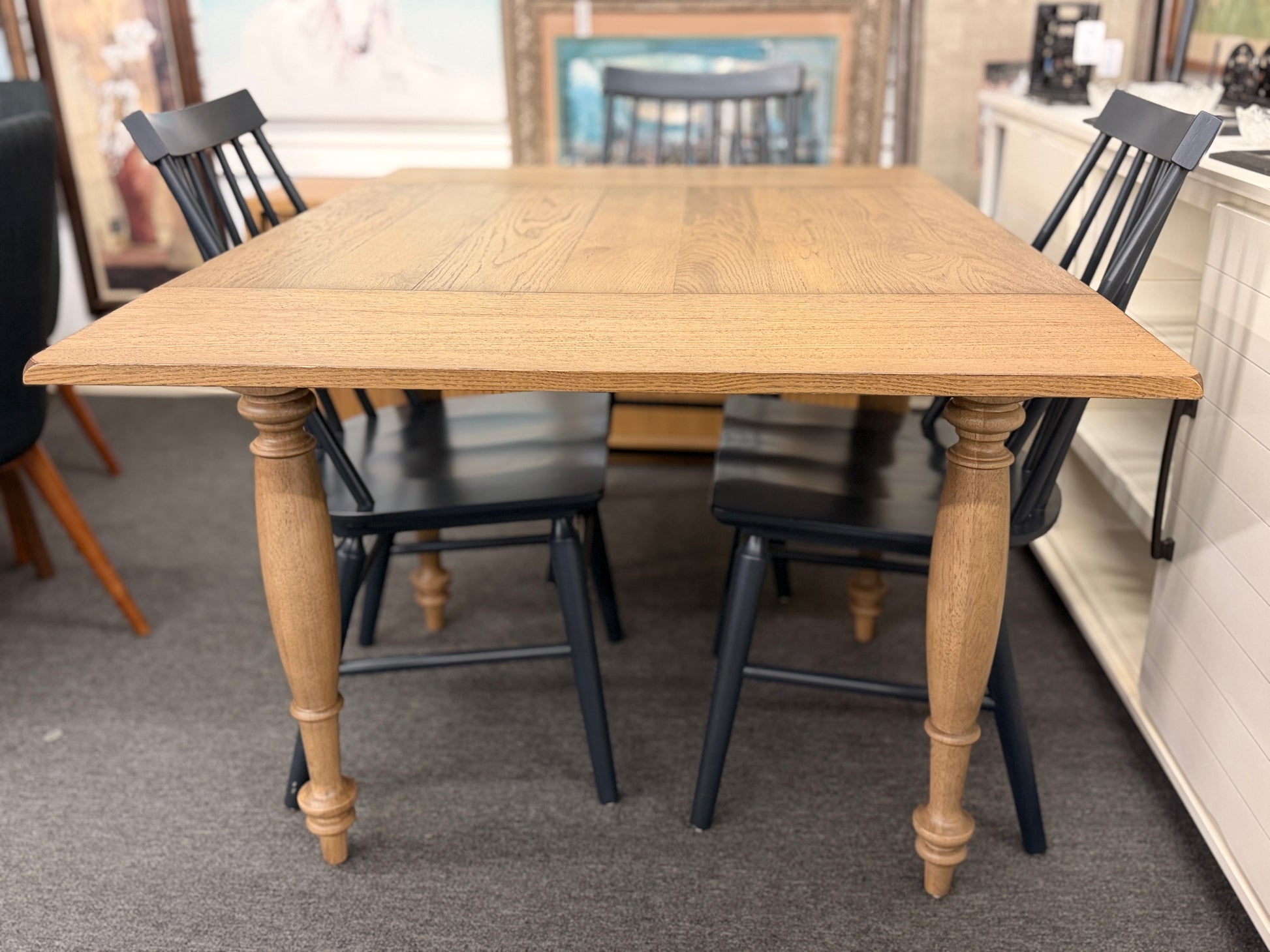 A farmhouse-style dining set featuring a rectangular light-wood extension table and four dark painted wooden Windsor-style chairs.