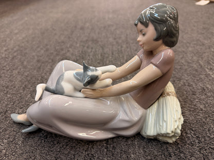 A fine porcelain figurine depicting a seated girl in a lavender-grey dress playing with a grey and white cat beside a sheaf of wheat in excellent condition.