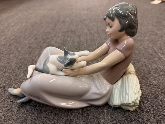 A fine porcelain figurine depicting a seated girl in a lavender-grey dress playing with a grey and white cat beside a sheaf of wheat in excellent condition.