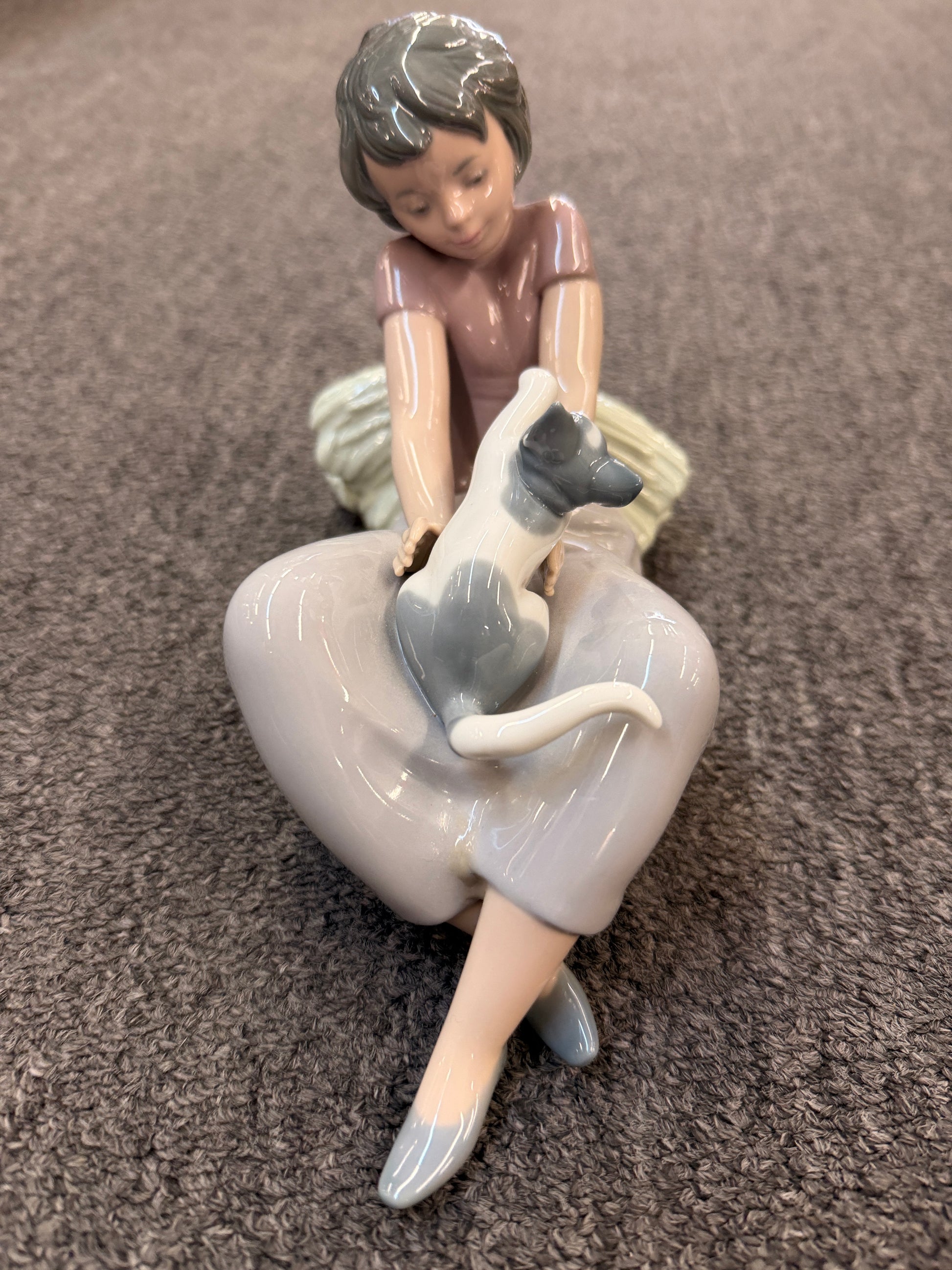 A fine porcelain figurine depicting a seated girl in a lavender-grey dress playing with a grey and white cat beside a sheaf of wheat in excellent condition.