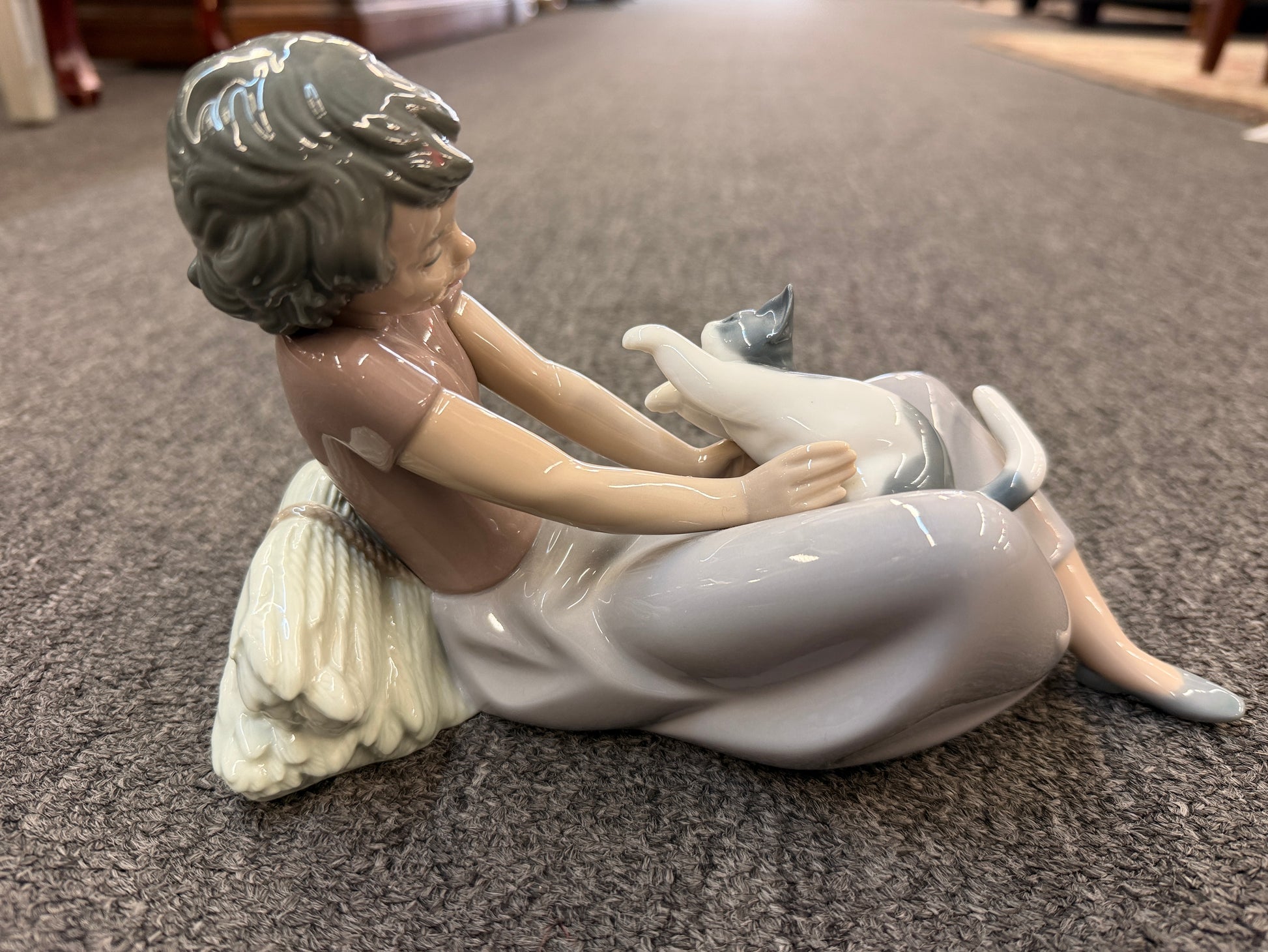 A fine porcelain figurine depicting a seated girl in a lavender-grey dress playing with a grey and white cat beside a sheaf of wheat in excellent condition.