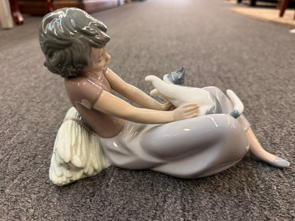 A fine porcelain figurine depicting a seated girl in a lavender-grey dress playing with a grey and white cat beside a sheaf of wheat in excellent condition.