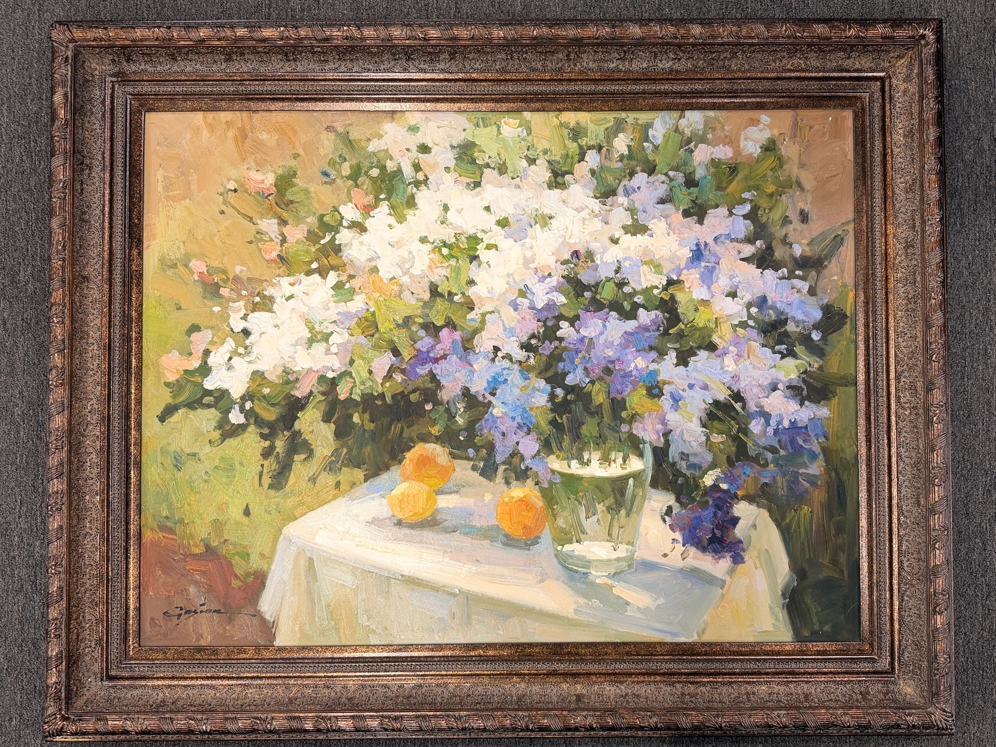A heavy-impasto floral painting featuring white and periwinkle flowers in a glass vase with citrus fruit in an ornate bronze frame in excellent condition.