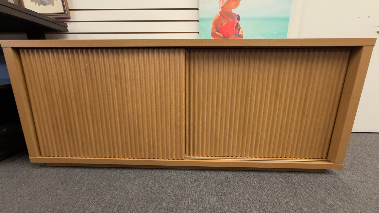 A low-profile minimalist TV stand cabinet featuring textured tambour-style vertical fluted sliding doors in good condition.