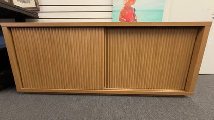 A low-profile minimalist TV stand cabinet featuring textured tambour-style vertical fluted sliding doors in good condition.