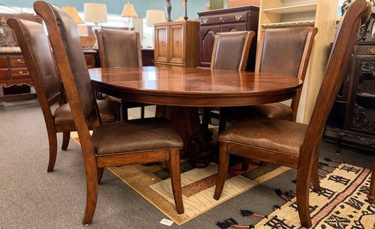 A formal 7-piece dining set featuring an oval dark wood extension table with a carved pedestal base and six upholstered high-back chairs with rolled silhouettes.
