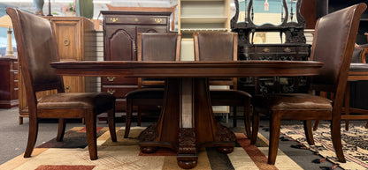 A formal 7-piece dining set featuring an oval dark wood extension table with a carved pedestal base and six upholstered high-back chairs with rolled silhouettes.