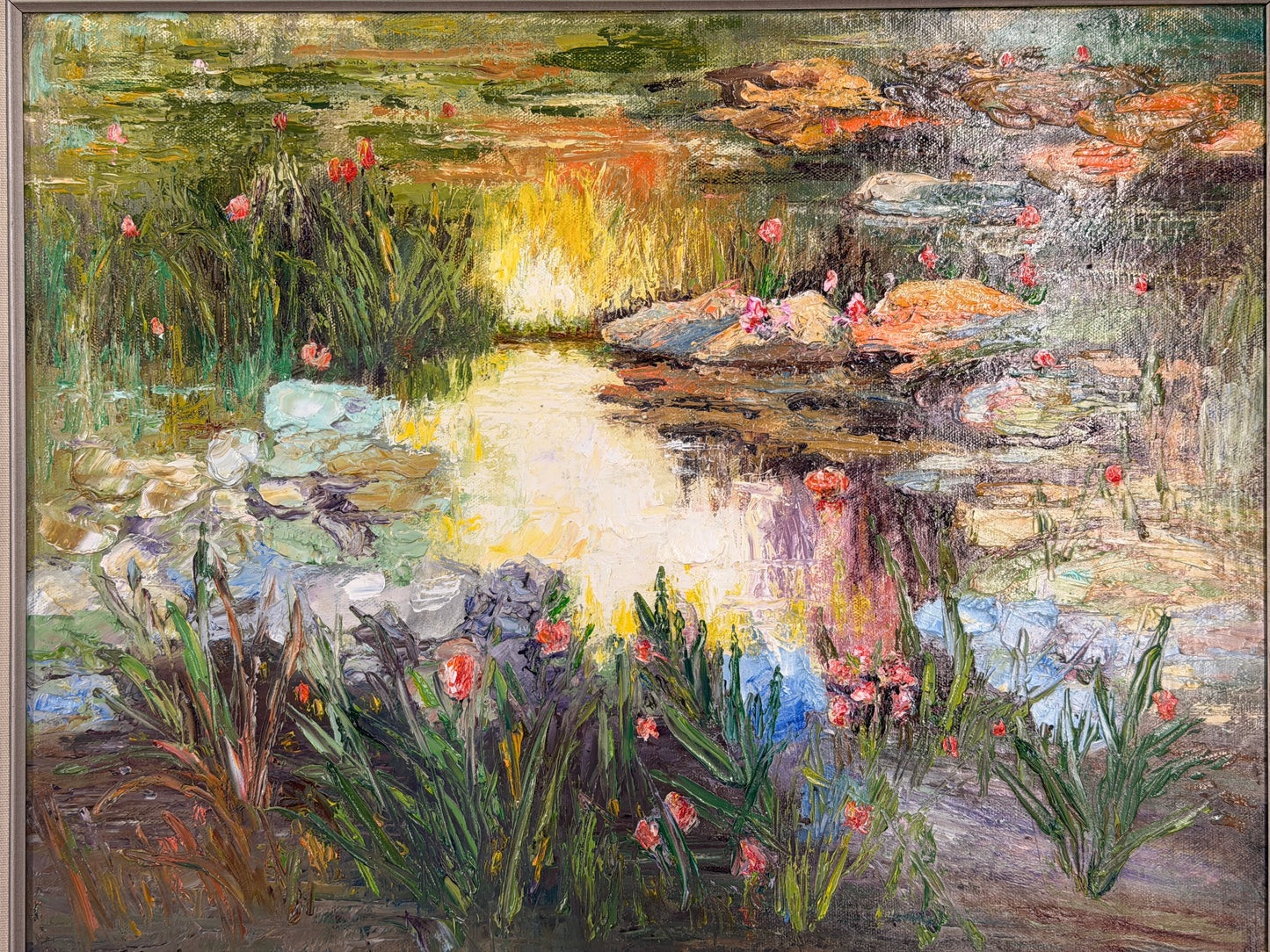 A framed Impressionist-style oil painting depicting a sunlit water lily pond, encased in a molded gray-blue and silver frame in excellent condition.