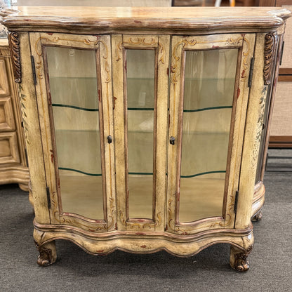 A French Provincial style three-door curio cabinet featuring a distressed antique cream finish, curved glass panels, and carved cabriole feet in excellent condition.