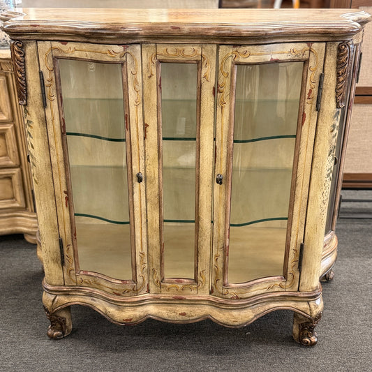 A French Provincial style three-door curio cabinet featuring a distressed antique cream finish, curved glass panels, and carved cabriole feet in excellent condition.