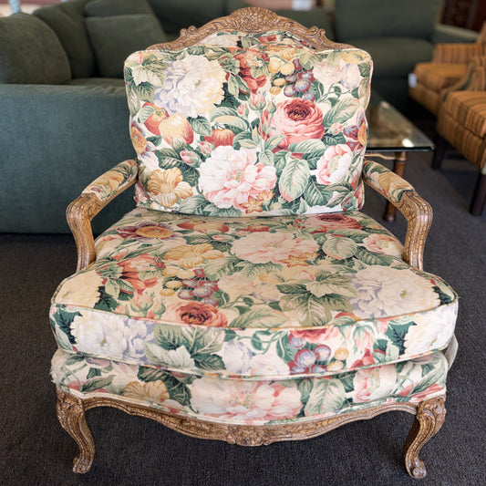 A French provincial-style armchair with an intricately carved exposed wooden frame, elegant cabriole legs, and vibrant multicolored floral fabric upholstery.