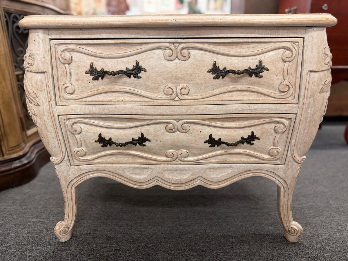 A French Provincial style two-drawer nightstand in a distressed antique-white finish featuring a serpentine front, cabriole legs, and ornate iron pulls.