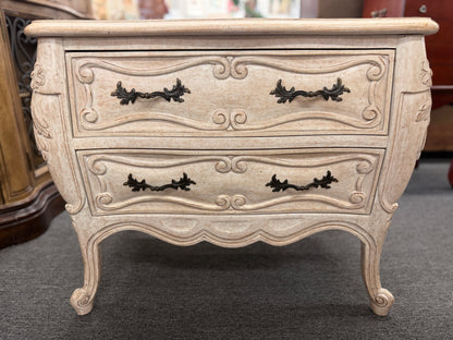 A French Provincial style two-drawer nightstand in a distressed antique-white finish featuring a serpentine front, cabriole legs, and ornate iron pulls.