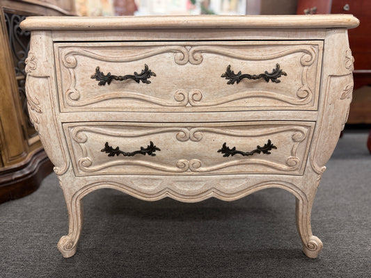 A French Provincial style two-drawer nightstand in a distressed antique-white finish featuring a serpentine front, cabriole legs, and ornate iron pulls.