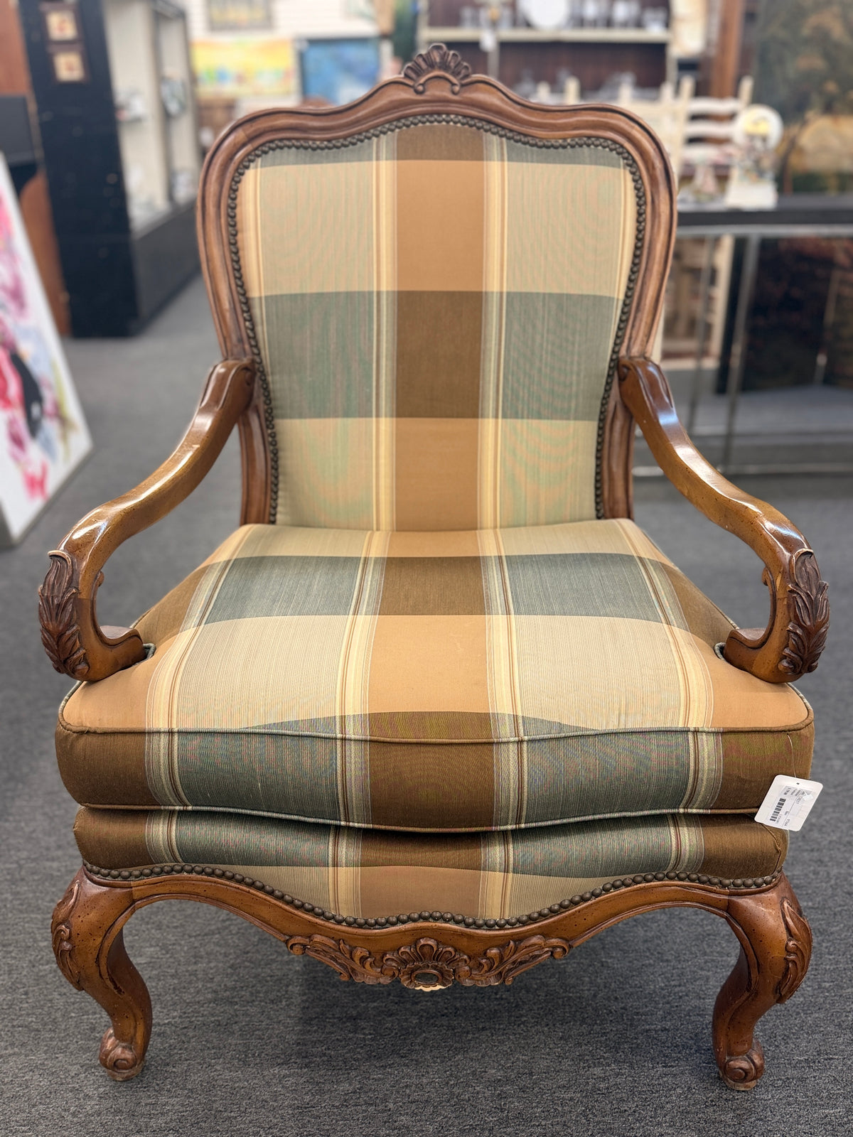 A French provincial-style armchair featuring a carved walnut frame, cabriole legs, nailhead trim, and plaid upholstery in earthy green, tan, and cream tones in good condition.