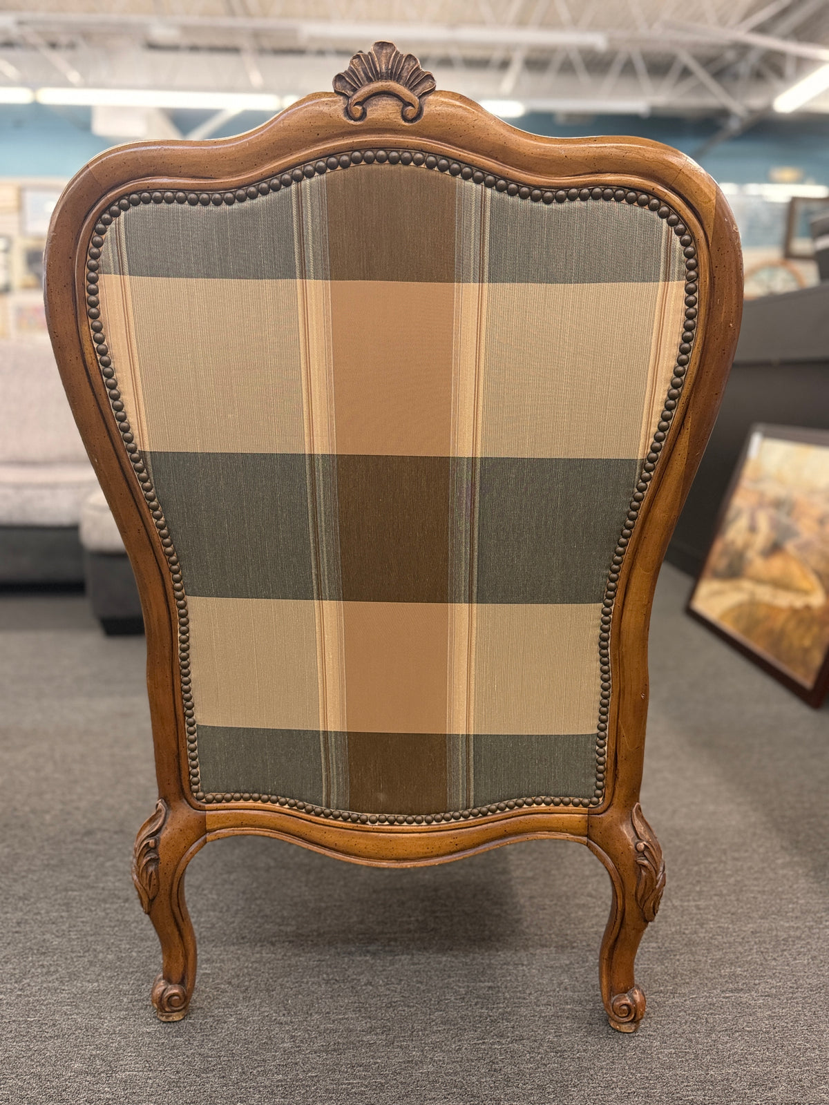 A French provincial-style armchair featuring a carved walnut frame, cabriole legs, nailhead trim, and plaid upholstery in earthy green, tan, and cream tones in good condition.