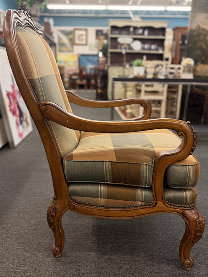 A French provincial-style armchair featuring a carved walnut frame, cabriole legs, nailhead trim, and plaid upholstery in earthy green, tan, and cream tones in good condition.
