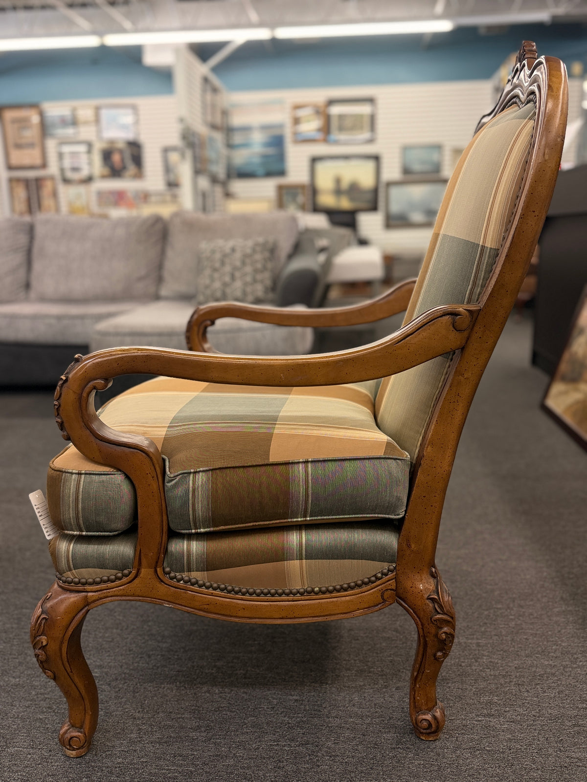 A French provincial-style armchair featuring a carved walnut frame, cabriole legs, nailhead trim, and plaid upholstery in earthy green, tan, and cream tones in good condition.