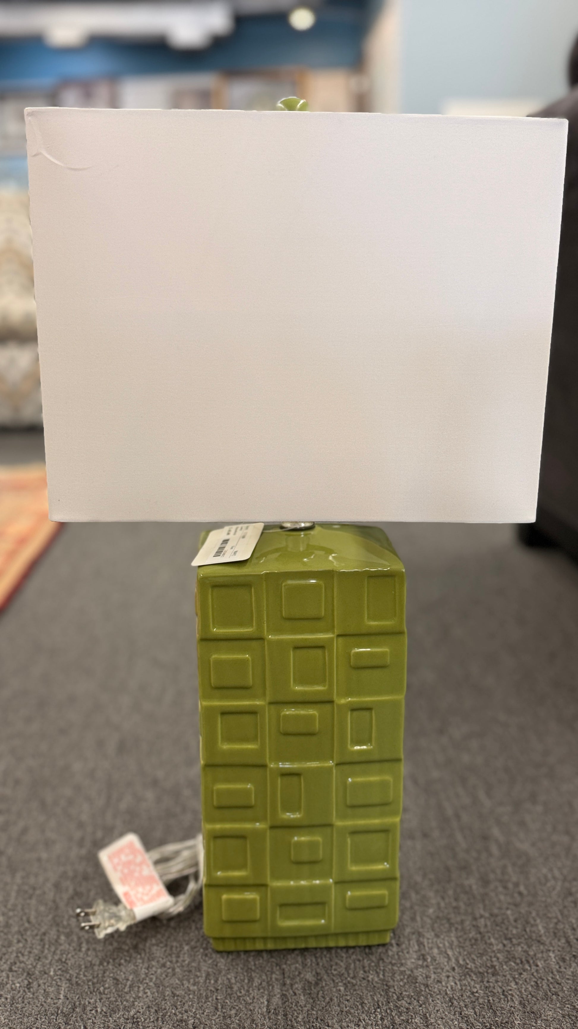 A rectangular table lamp featuring a glossy green ceramic base with a raised geometric block pattern and a white fabric rectangular shade.