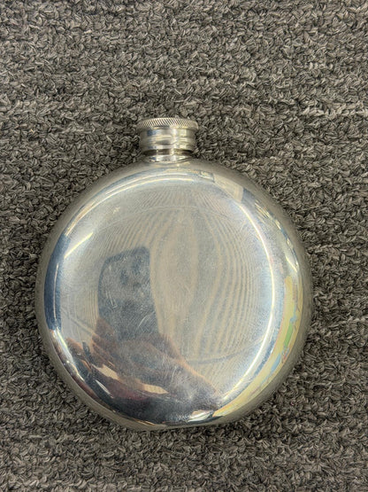 A circular pocket hip flask featuring a central scrimshaw-style engraving of a golfer mid-swing in excellent condition.