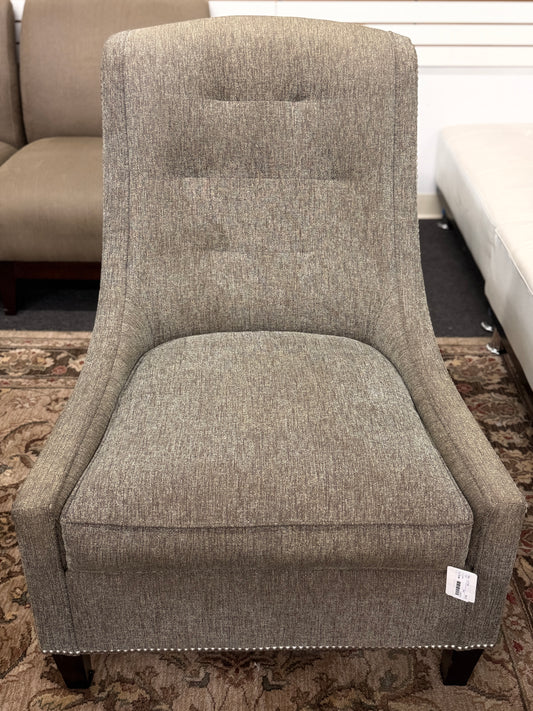 Gray upholstered armless accent chair featuring textured fabric, a gently curved tufted back, silver nailhead trim, and dark wooden legs.