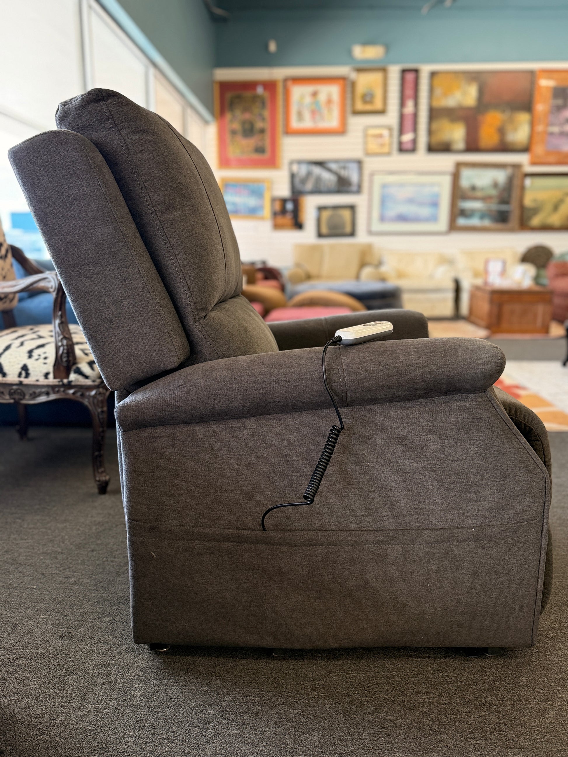 A standard upholstered recliner chair in a solid grayish-brown fabric featuring a structured paneled backrest and padded armrests.