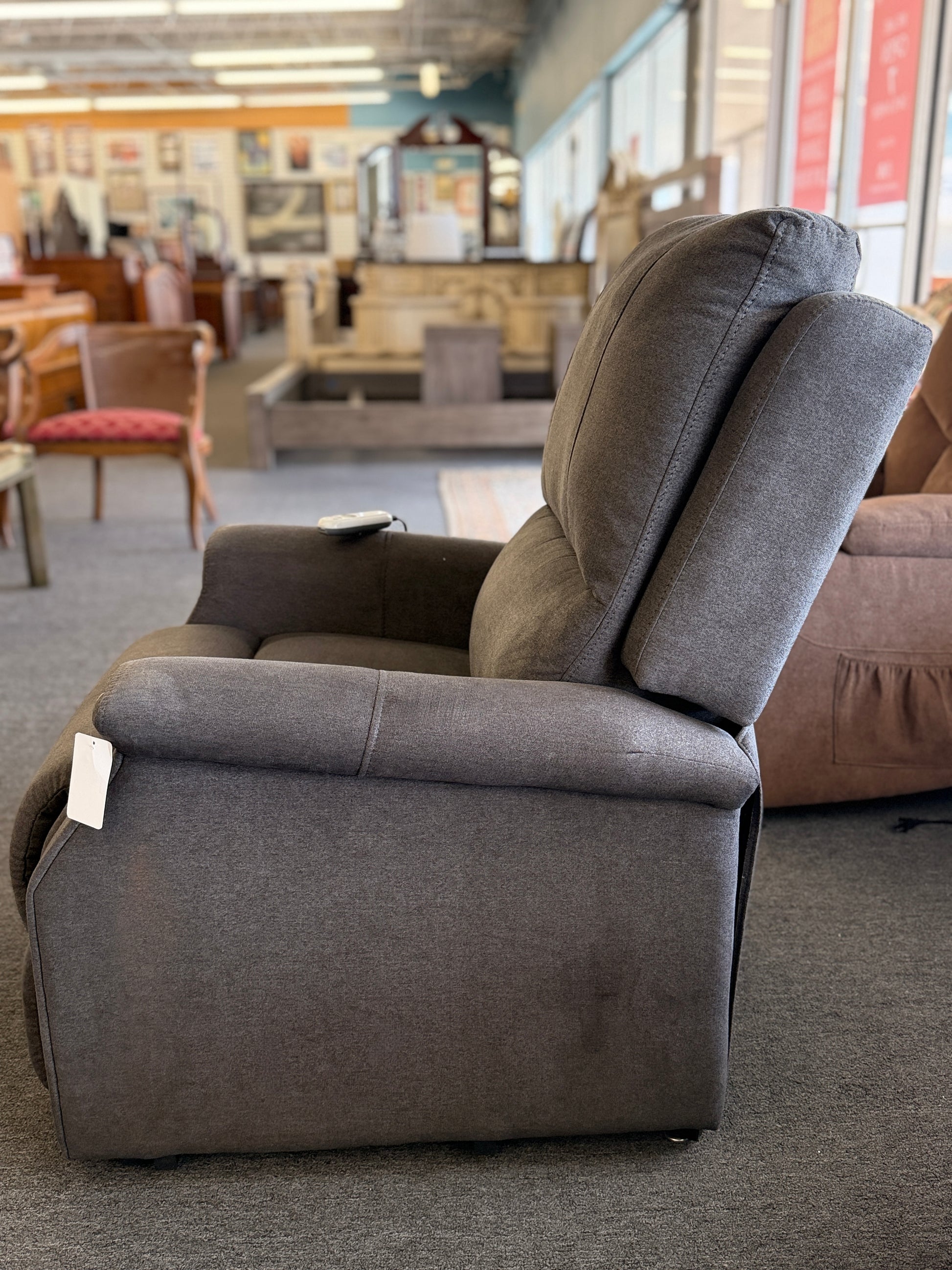 A standard upholstered recliner chair in a solid grayish-brown fabric featuring a structured paneled backrest and padded armrests.