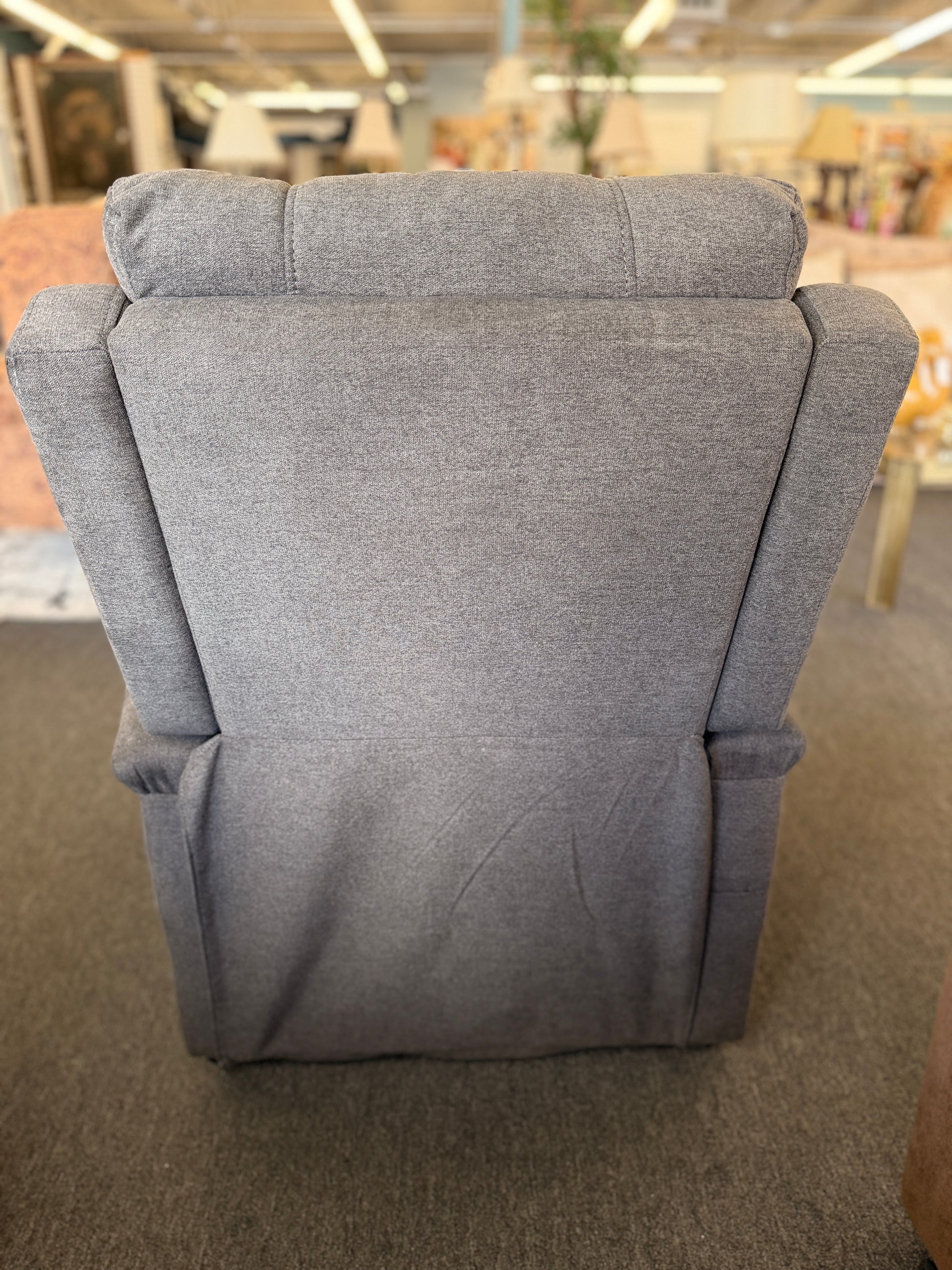 A standard upholstered recliner chair in a solid grayish-brown fabric featuring a structured paneled backrest and padded armrests.