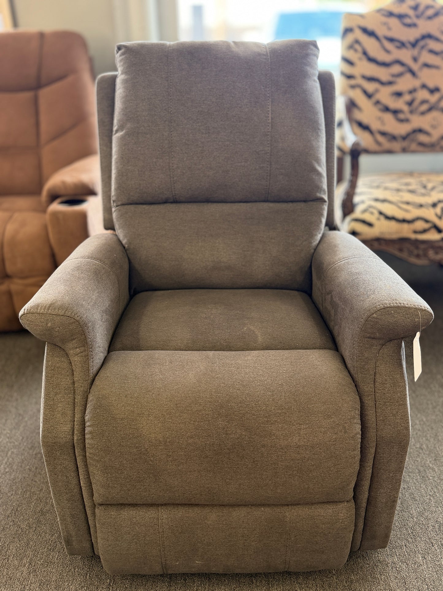 A standard upholstered recliner chair in a solid grayish-brown fabric featuring a structured paneled backrest and padded armrests.