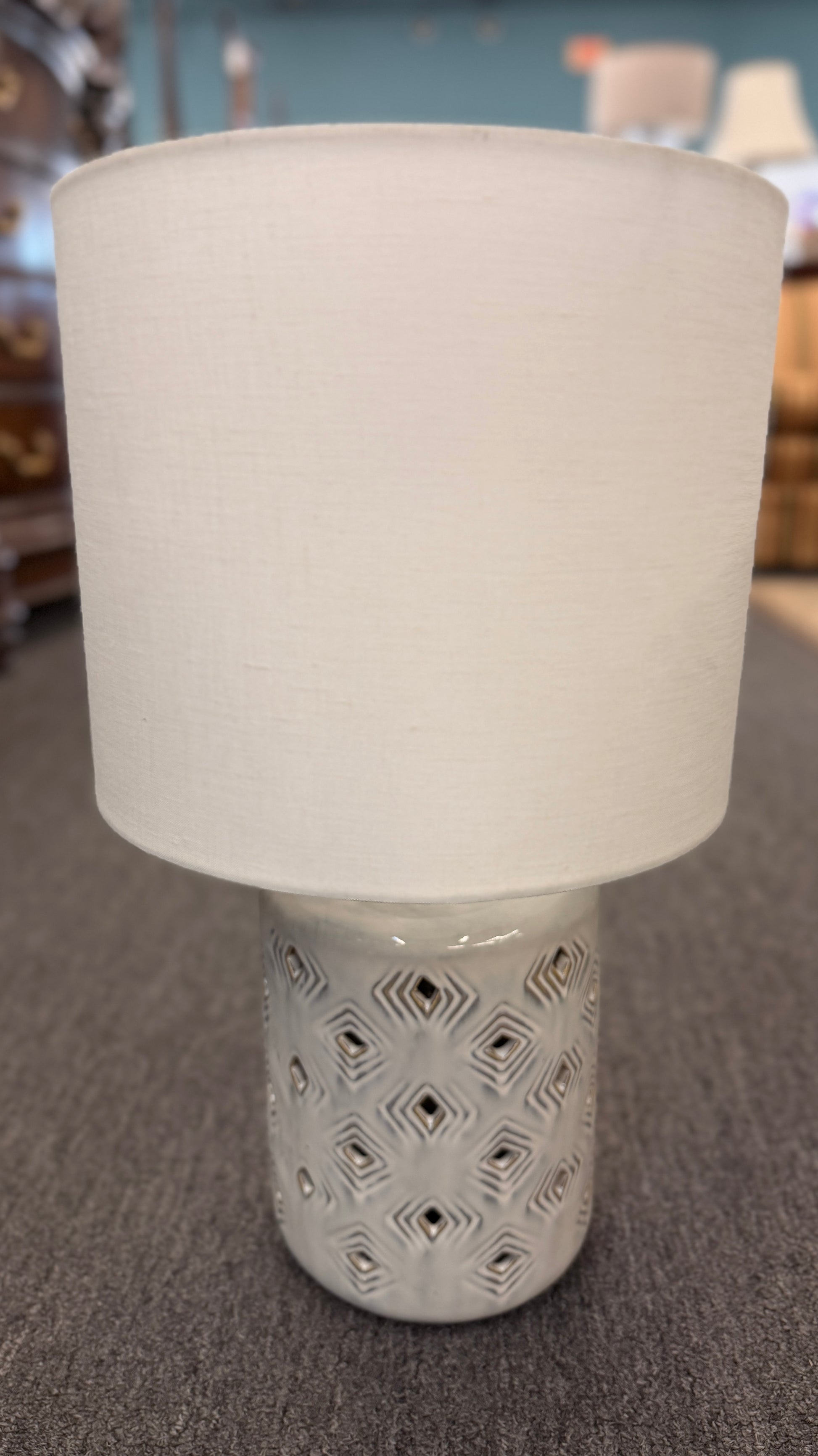 Modern grey geometric diamond cutout ceramic table lamp featuring a textured base and a white drum shade on a gray surface at 2nd Debut Houston consignment showroom