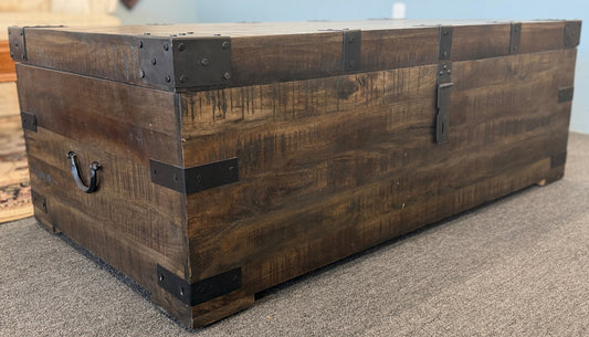 A rustic industrial trunk coffee table made of distressed dark wood with black iron corner brackets, open partially to reveal a lift-top mechanism and internal storage space.
