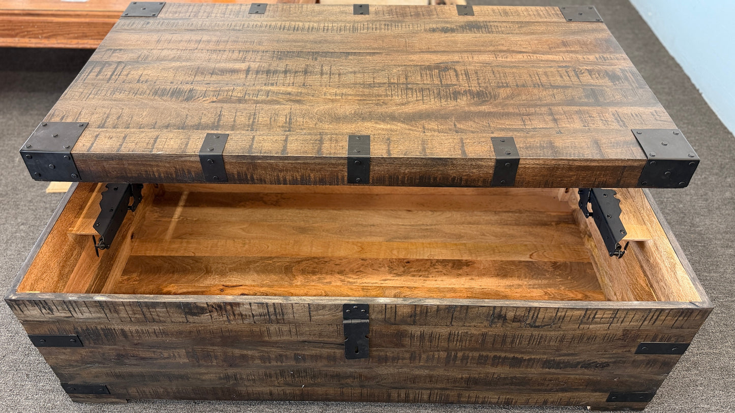 A rustic industrial trunk coffee table made of distressed dark wood with black iron corner brackets, open partially to reveal a lift-top mechanism and internal storage space.