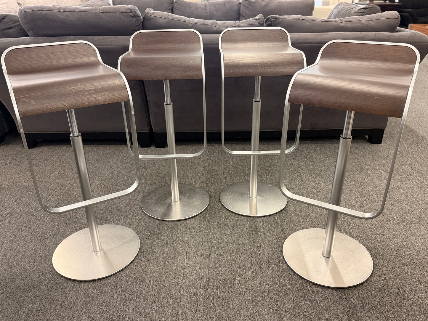 A set of four contemporary Lapalma-style adjustable barstools featuring curved bentwood scoop seats, metal frames, integrated footrests, and heavy disc bases in good condition.
