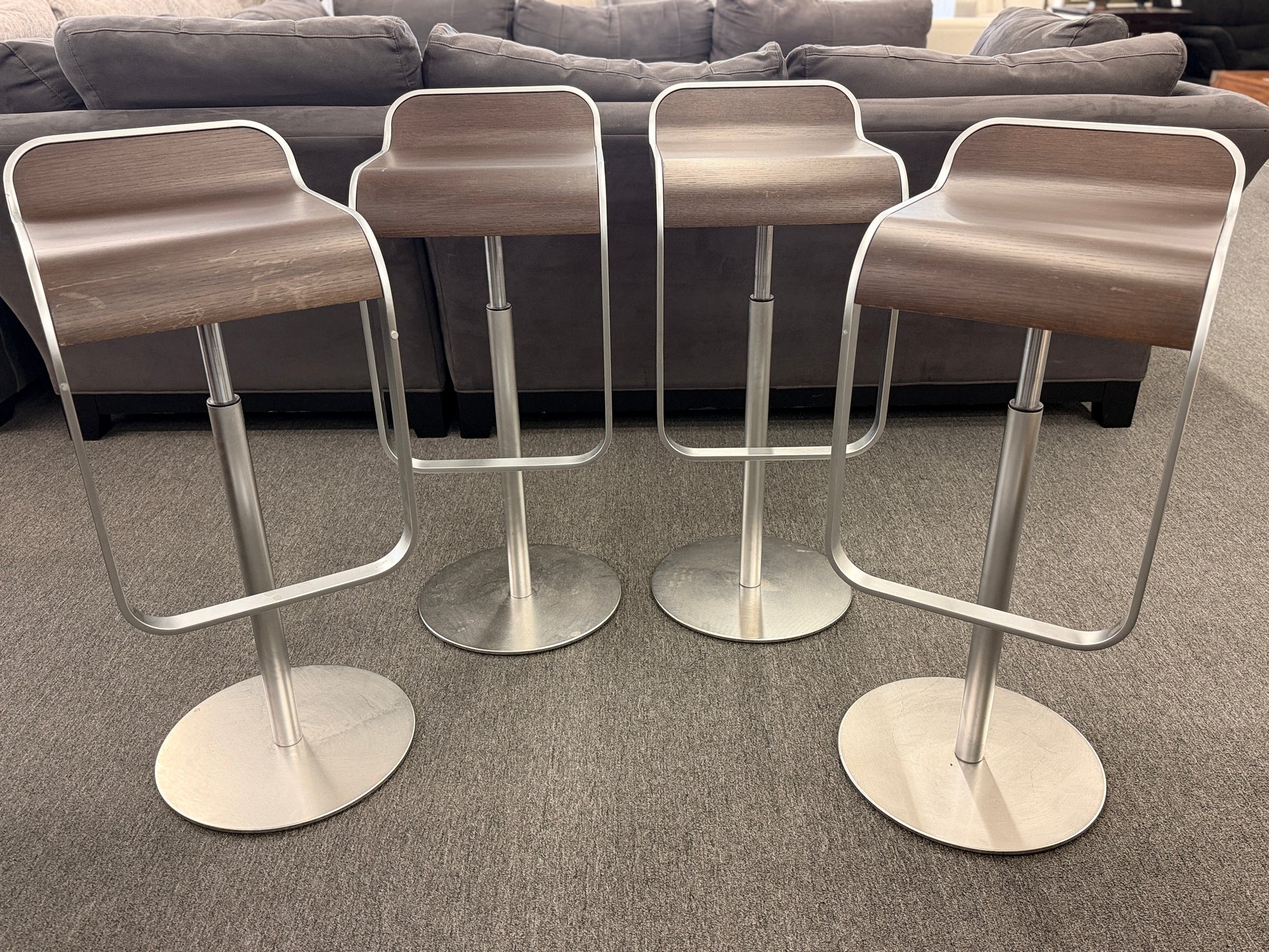 A set of four contemporary Lapalma-style adjustable barstools featuring curved bentwood scoop seats, metal frames, integrated footrests, and heavy disc bases in good condition.