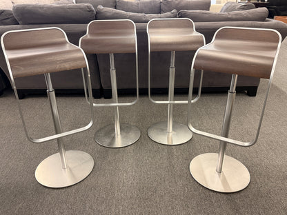 A set of four contemporary Lapalma-style adjustable barstools featuring curved bentwood scoop seats, metal frames, integrated footrests, and heavy disc bases in good condition.