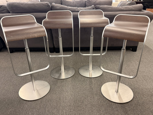A set of four contemporary Lapalma-style adjustable barstools featuring curved bentwood scoop seats, metal frames, integrated footrests, and heavy disc bases in good condition.