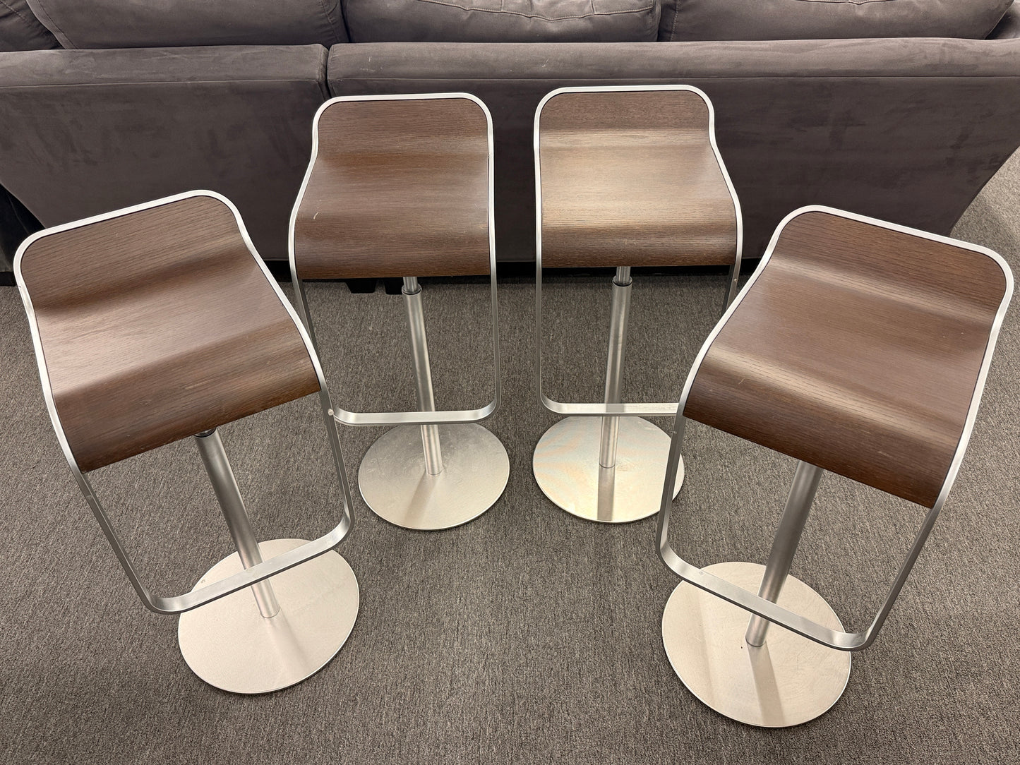 A set of four contemporary Lapalma-style adjustable barstools featuring curved bentwood scoop seats, metal frames, integrated footrests, and heavy disc bases in good condition.